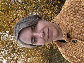  a woman with short hair in an orange sweater in front of trees with yellow leaves